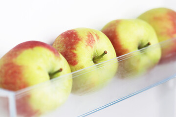 Apples in fridge. Isolated on white fridge door. Fresh green and red apples with small natural spots. Ripe bunch of apples on a transparent refrigerator shelf and in a plastic fridge drawer.