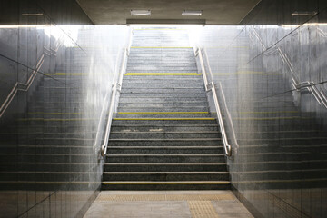 Underground tunnel stairs under train tracks with a bright end. Illuminated passageway leading to stairs. Urban transit infrastructure. Train station platform entrance background. Stairway to light.