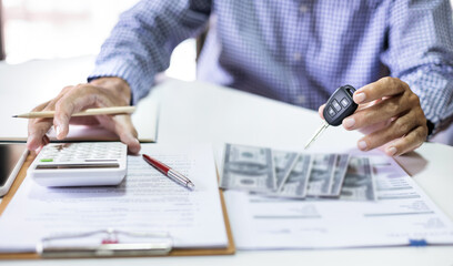 Men's hand holding car key reviewing personal loan contract and car accident insurance calculate...