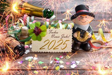 Wooden hang tag and slate with four leaf clover and sparklers with the german words for happy new year - frohes neues jahr 2025 on wooden weathered background	