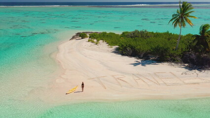 Aerial view of a woman walking on a tropical beach with travel written in the sand, enjoying a...