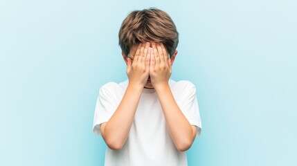 Boy Hiding His Face with Hands Against a Blue Background