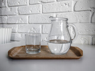 glass jug and glass with water on wooden tray against white brick wall in scandinavian style