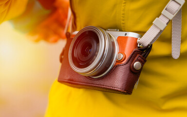 Close-up of a vintage-style camera in a leather case, worn over the shoulder of a person dressed in a yellow jacket. The warm sunlight creates a nostalgic and inviting atmosphere, perfect for promotin