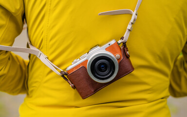 Modern mirrorless camera in a stylish leather case, hanging on a strap over a vibrant yellow jacket. The minimalist composition highlights the camera’s design and the contrasting colors make