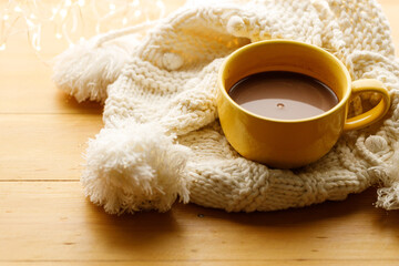 Cup of delicious hot chocolate on warm sweater on wooden table background. Selective focus.