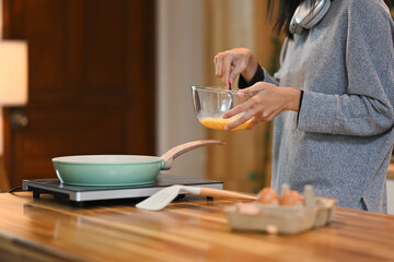 Cropped shot of young woman beating eggs in a bow with fork, making breakfast in the kitchen