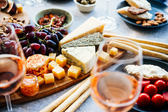 Wooden board with different kinds of cheese and glass of rose wine. Dinner or aperitivo party concept.