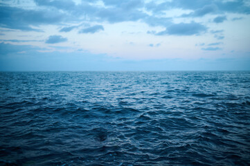 Tranquil ocean waves gently lap at the shore during sunset under a cloudy sky, creating a peaceful...