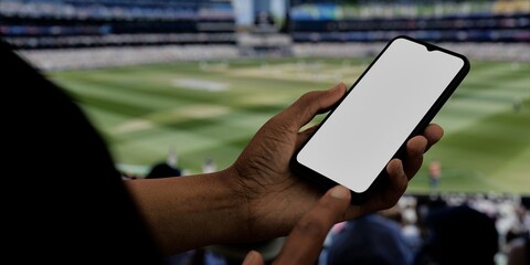 Black African-American male using smartphone with a blank white screen. Cricket, stadium, sport apps mockup. Vertical phone orientation