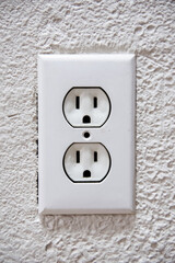 An American 110 volt three prong electrical power outlet isolated on rough textured white wall.