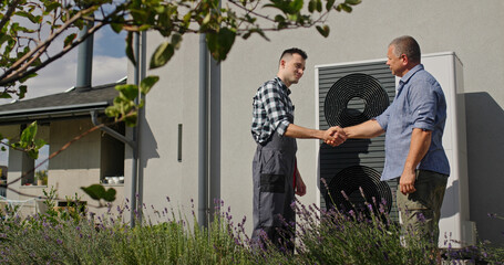 A technician and a homeowner shake hands beside an external heat pump, concluding a service visit.