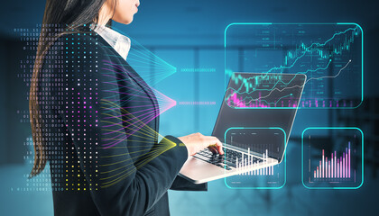 Businesswoman using a laptop with financial data and holographic charts in the background.