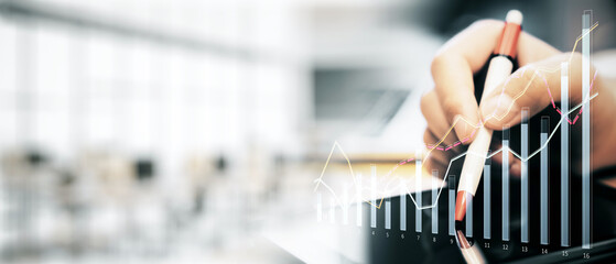 Businessman's hand holding a pen with financial graph overlay, in a blurred office background.