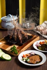 Satay: A stack of skewered satay served on a small black plate. The plate is placed on a mini wooden grill, adding a warm and authentic feel to the dish.