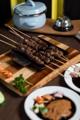 Satay: A stack of skewered satay served on a small black plate. The plate is placed on a mini wooden grill, adding a warm and authentic feel to the dish.