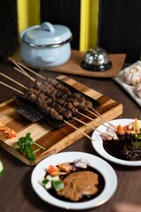 Satay: A stack of skewered satay served on a small black plate. The plate is placed on a mini wooden grill, adding a warm and authentic feel to the dish.