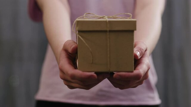 Slow motion young woman stand and show brown gift box with twine bow