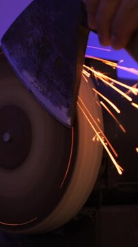 vertical video Blacksmith sharpening axe blade using grinding machine