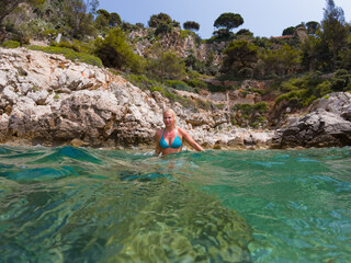 A young blonde woman tourist in a bikini in the water on the wild beach de la Gavinette in France on a summer day.