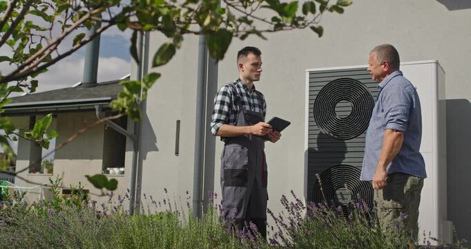 A technician and a homeowner shake hands beside an external heat pump, concluding a service visit.