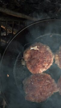 Vertical video of burger patties fried on hot pan at autumn nature. Process of cooking juicy mouth-watering burgers at outdoors. Fast food concept