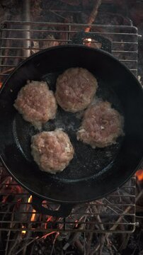 Vertical footage of four burger patties fried on hot pan in nature. Process of cooking juicy mouth-watering burgers at outdoors. Fast food concept