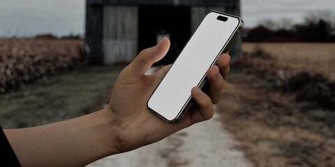 Caucasian White male using smartphone with a blank white screen. Rustic barn, farm, tractor inside barn apps mockup. Vertical phone orientation