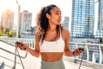 Portrait of a beautiful sporty woman doing a workout on the street with a jump rope. Motivation, fitness exercises and morning cardio.