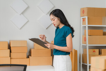 E-commerce Efficiency: Young Asian entrepreneur meticulously checks inventory in her bustling...