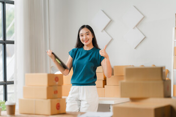 E-commerce Success:  A young Asian entrepreneur celebrates her thriving business, surrounded by packages and giving a thumbs-up, embodying the excitement of online retail.  