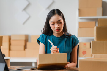 E-commerce Efficiency: Young Asian entrepreneur meticulously addresses a package, embodying the...