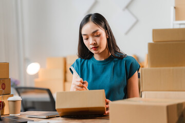 Shipping Success: A young Asian entrepreneur meticulously addresses a package in her bustling home...