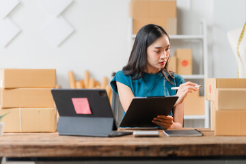 E-commerce Efficiency: Young Asian entrepreneur meticulously manages orders in her bustling home...