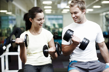Fototapeta premium Couple, smile and exercise with weights in gym for bodybuilding, fitness and training together. Man, woman and happy with equipment in health club for strength workout, support or teamwork in morning