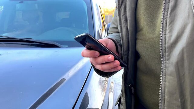 Man buyer client using phone app,wants to buy new car,parking vehicle,typing,chatting surfing internet,purchasing near auto.Mobile application for electric automobile.
