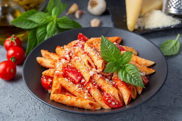 Classic italian pasta penne alla arrabiata with basil and freshly grated parmesan cheese on dark table. Penne pasta with chili sauce arrabbiata.