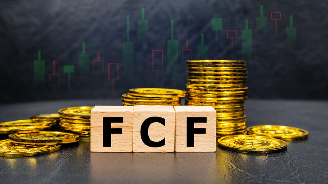 The inscription FCF text on wooden cubes with stack of coin on black background with stock market graph. Business profitability success growth profitability analytics. Business and financial concept.