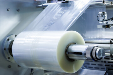 roll of plastic packaging film on the automatic packing machine in food product factory. industrial and technology concept.