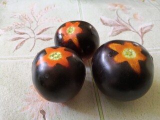 The photo shows three black cherry tomatoes with characteristic dark purple skin. They have bright orange star-shaped markings near the base of the stem, giving them a unique appearance. The tomatoes 