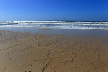 A tranquil scene of the Atlantic Ocean along the coast of Portugal, with waves breaking against a rocky barrier and grass-covered dunes overlookin