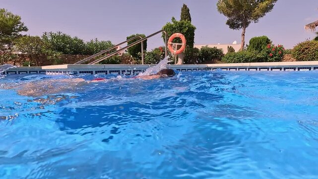 Girl swimming crawl style in a pool seen from above the water surface in a natural setting with palm trees and trees