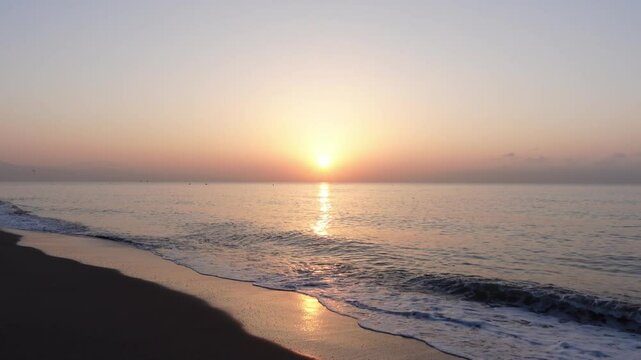 A serene sunrise or sunset over a calm Mediterranean sea, with the sun casting a warm glow on the horizon at golden hour, creating a peaceful and tranquil atmosphere, seen from the coastline