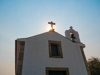 Sun rising behind stone cross on an old, historic Catholic church in rural Portugal, in the early morning. View from below.