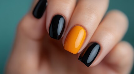 Fototapeta premium A close-up of a hand showcasing a manicure with glossy orange and black nails, reflecting a bold and stylish fashion statement suitable for modern trends and aesthetics.