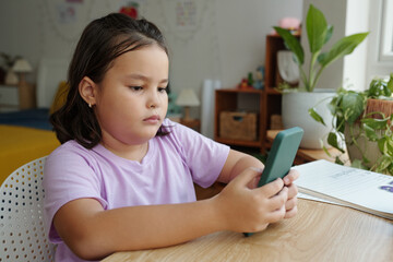 Girl sitting at desk in her room and using smartphone during studying