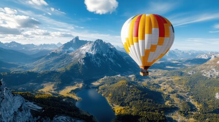 Fototapeta premium A vibrant orange and yellow hot air balloon floats above the rugged mountain landscape, offering a stunning aerial view of the dense greenery and distant peaks under a crisp blue sky.