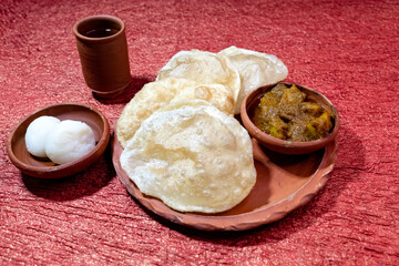 Bengali traditional and most common breakfast or snack 'Luchi' or 'Poori' or deep-fried flatbread. Served with spicy potato curry and indian dessert rosogolla in earthenware