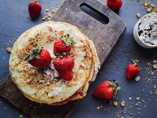 Pancakes with cream and strawberries on wooden board and dark rustic background
