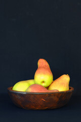 Freshly harvested pears displayed in a rustic wooden bowl against a dark background
